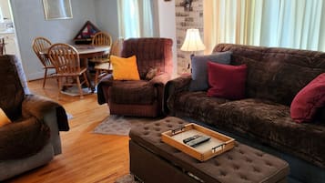 A cozy living room with a brown sofa, a matching ottoman, and a dining area with wooden chairs and a table.