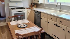 Keittiössä on liesi, pesuallas ja puinen ruokapöytä tuoleineen.