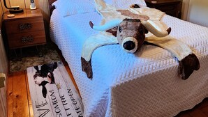 Makuuhuone, jossa on sänky, lamppu, yöpöytä, laatikko, taulu ja tekstillä varustettu matto.