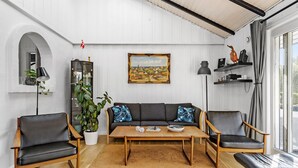 Ein Wohnzimmer mit einer Couch, zwei Sesseln, einem Couchtisch, einer Topfpflanze, einem Gemälde und einem Bücherregal.