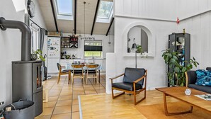 Eine moderne Küche mit einer zentralen Kochinsel, ein Essbereich mit Tisch und Stühlen, eine gemütliche Sitzecke mit Sofa und Sessel, sowie ein großes Fenster, das für natürliches Licht sorgt.