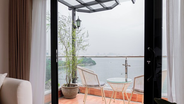 Ein Balkon mit Blick auf ein Gewässer, Korbstühle, ein Glastisch und ein Blumentopf.