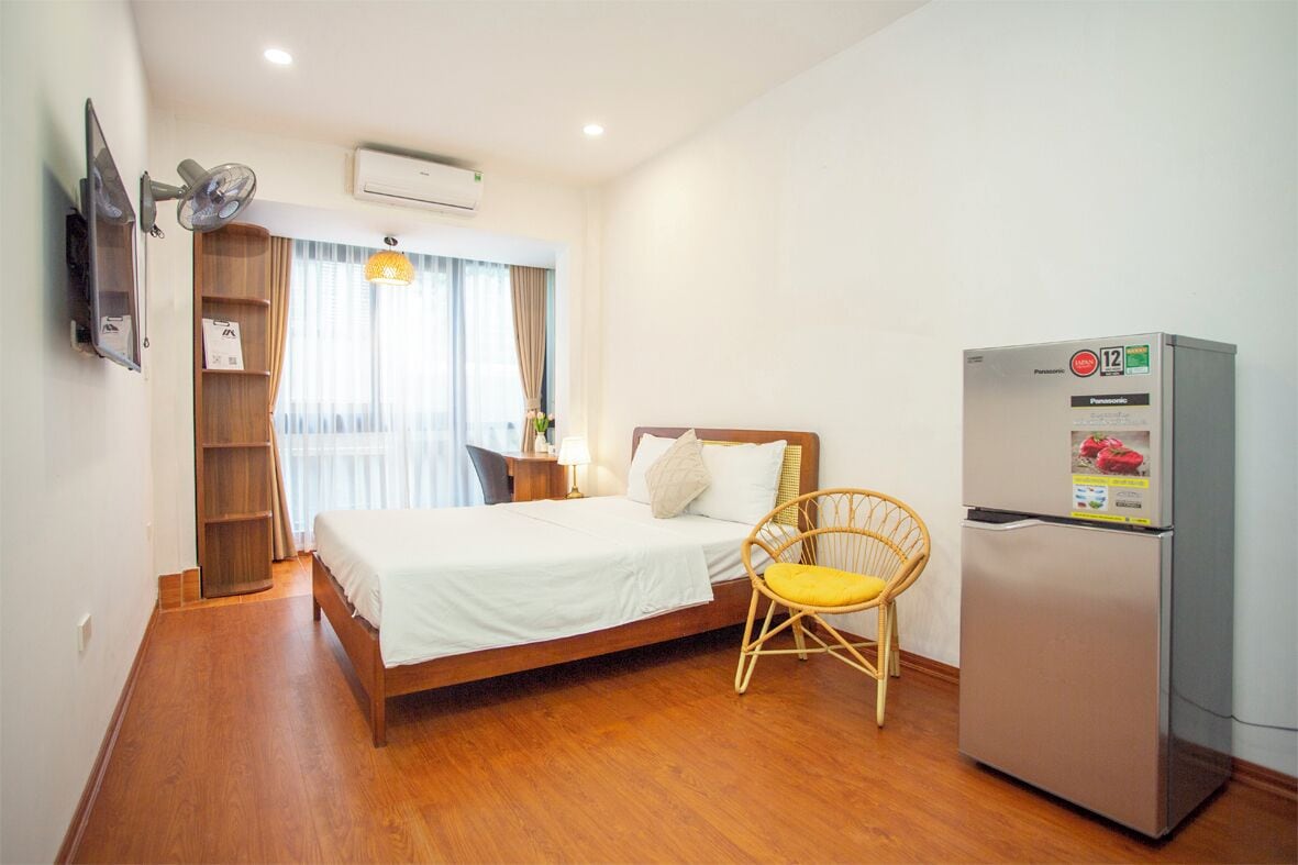 Une chambre d’hôtel avec un lit, un plancher en bois, un réfrigérateur, une chaise, une télévision et une étagère.