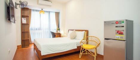 Une chambre d’hôtel avec un lit, un plancher en bois, un réfrigérateur, une chaise, une télévision et une étagère.