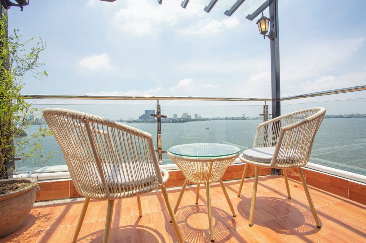 A balcony with wicker chairs and a glass table overlooking a body of water with a city skyline in the distance.