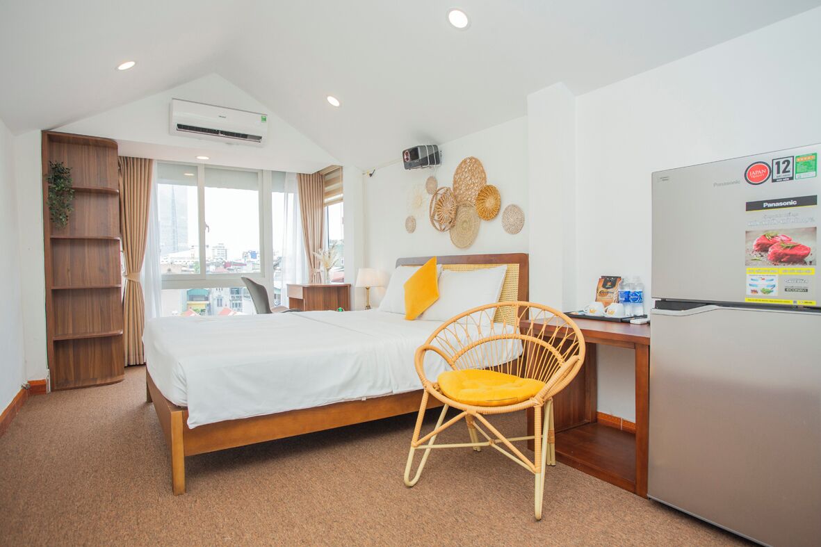 A hotel room with a bed, a wooden chair, a desk, a refrigerator, and a wall-mounted air conditioner.