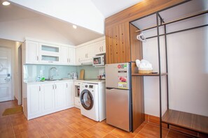 Una cocina moderna con armarios blancos, lavadora, refrigerador y estante de madera.