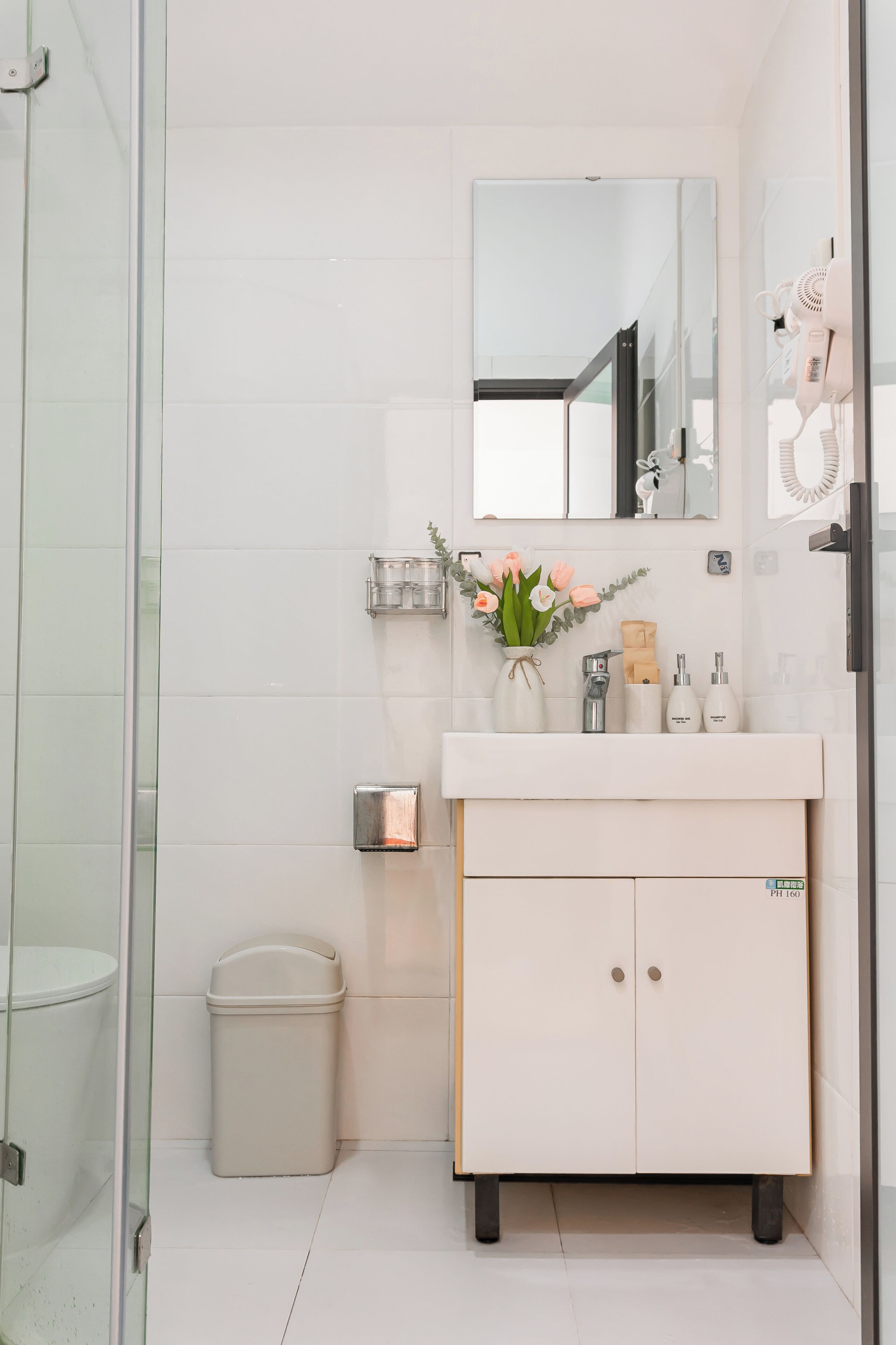 A modern bathroom with a glass shower enclosure, a white vanity with a mirror, and a trash bin.