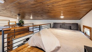 A bedroom with a wooden ceiling, a bed with a beige blanket, a grey pillow, and a black and white patterned pillow. - Charming Tiny Home Cottage - East Side! (Austin)
