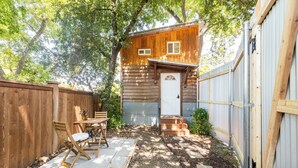 A wooden cabin with a white door, a patio with chairs, and a fenced yard. - Charming Tiny Home Cottage - East Side! (Austin)