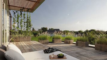 A wooden deck with a white sofa and cushions, surrounded by planters with greenery, and a view of a house in the background.