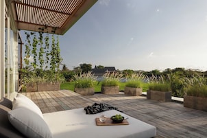 A wooden deck with a white sofa and cushions, surrounded by planters with greenery, and a view of a house in the background.
