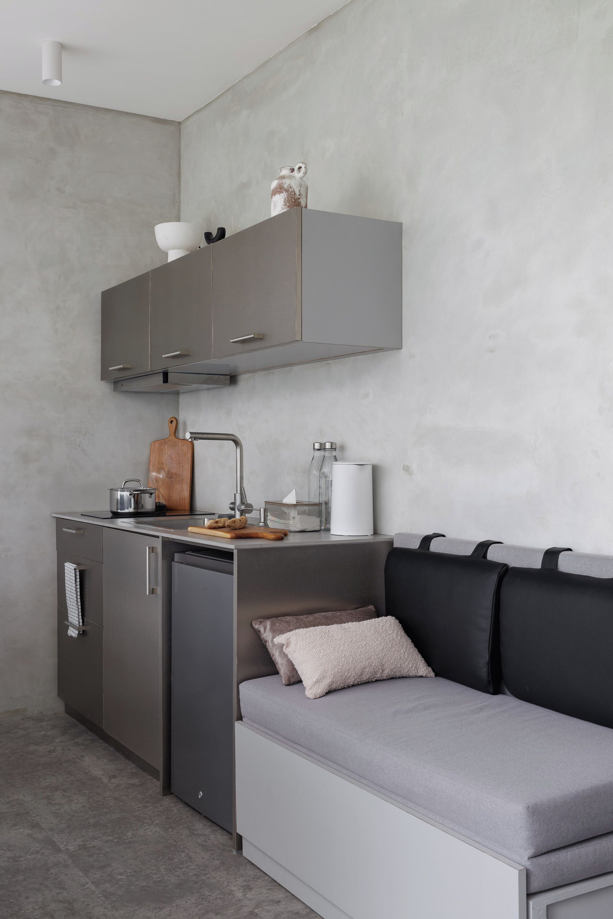 Una kitchenette compacta con horno empotrado, un lavamanos y una tabla de cortar de madera.