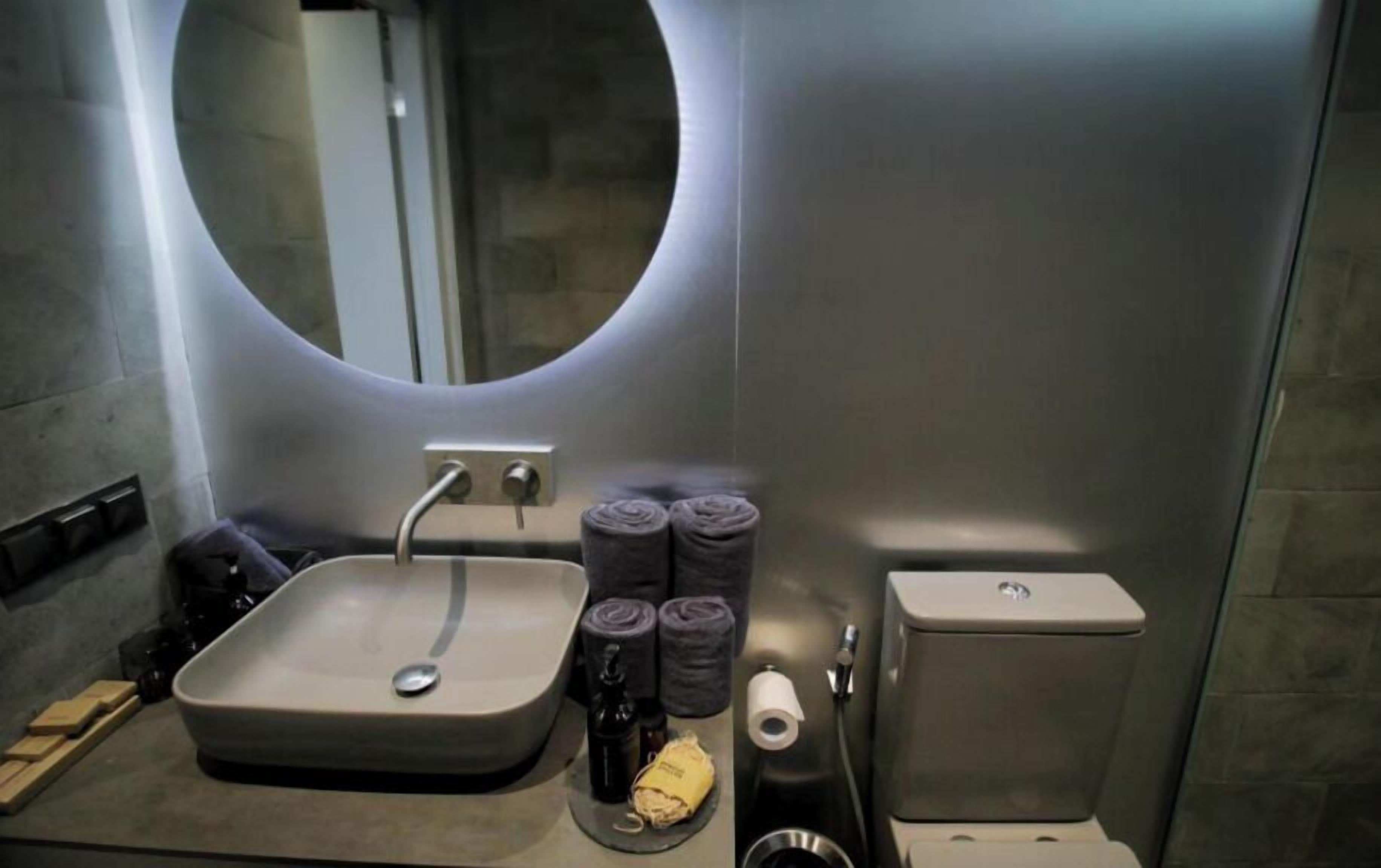 A modern bathroom with a rectangular sink, a round mirror, and a toilet.