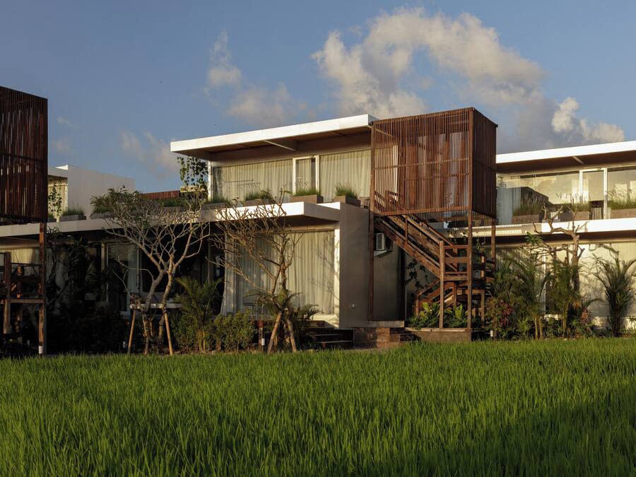 A modern house with a large balcony, a staircase, and a lush garden.