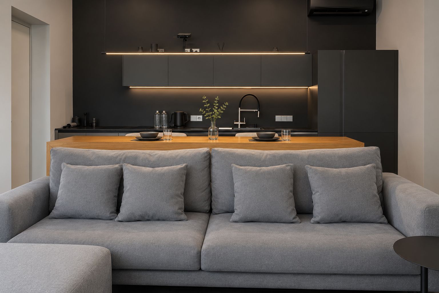 A modern kitchen with a central island, grey sofa, and a small side table.