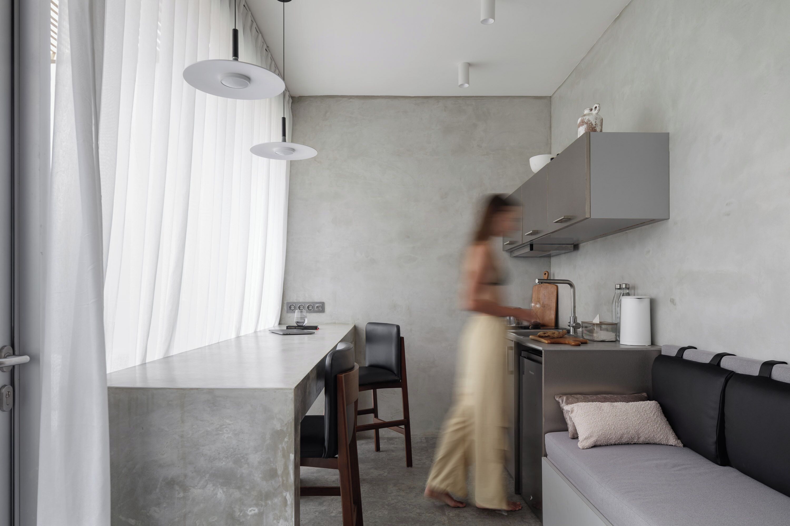 A modern kitchen with a grey countertop, a built-in oven, and a grey sofa with cushions.