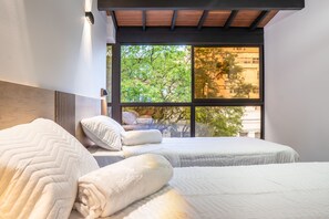 A bedroom with two beds, a large window, and a view of trees and buildings outside.