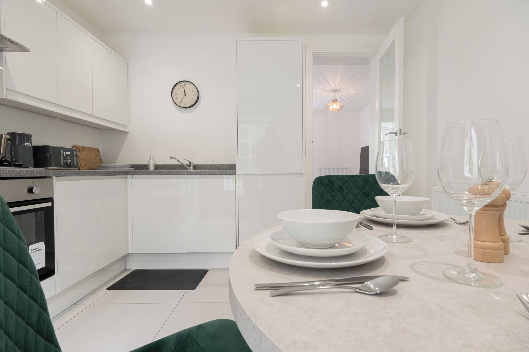 A modern kitchen with white cabinets, a sink, and a dining area set with plates, bowls, and wine glasses.