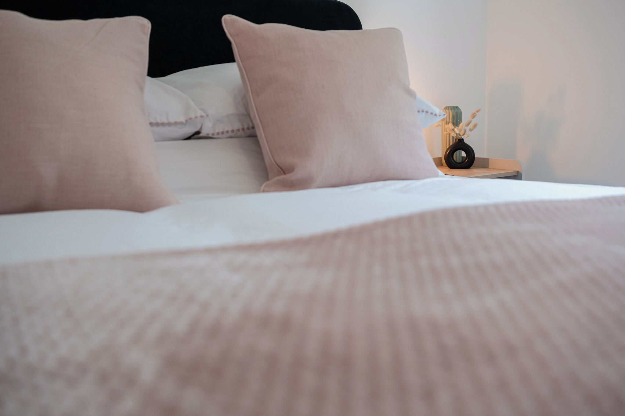 A neatly made bed with a white comforter and two pink pillows.