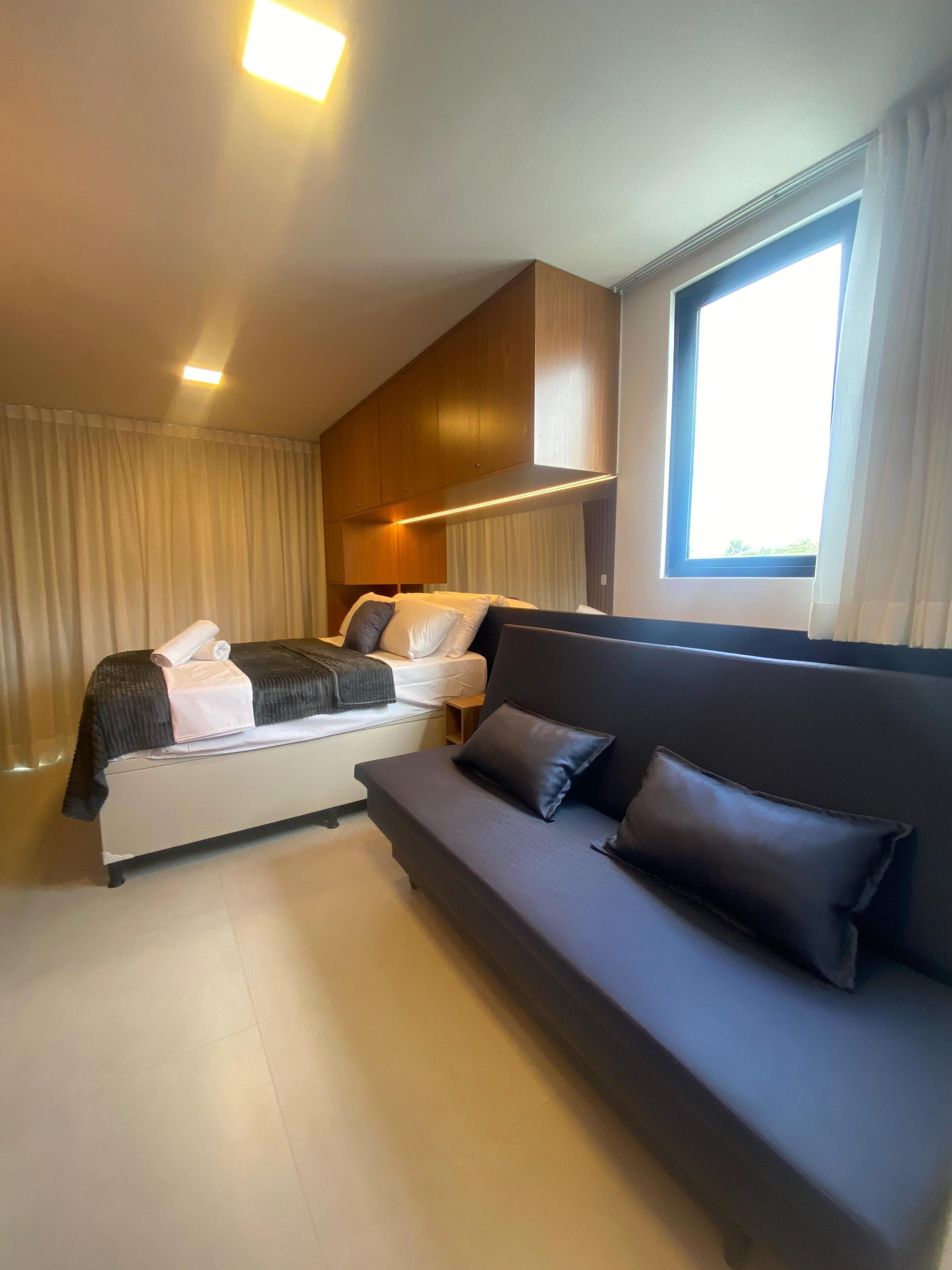 Ein modernes Schlafzimmer mit einem Bett, einer Couch und einem großen Fenster.