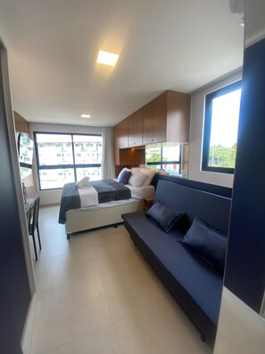 Une chambre d’hôtel compacte comprenant un lit, un canapé, un bureau et une grande fenêtre donnant sur la ville.
