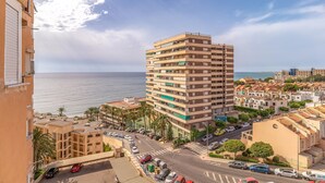A multi-story building with balconies, a street in front, and a view of the sea.