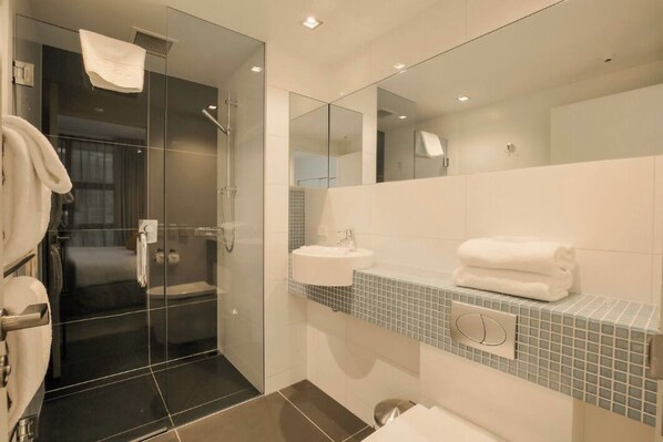 Un baño moderno con ducha envuelta en vidrio, un lavamanos blanco y un espejo grande.