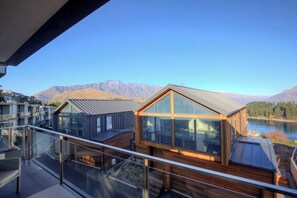 Un edificio moderno con fachada de vidrio y terraza de madera con vistas a un lago y montañas.