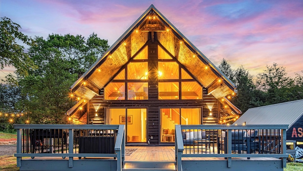 Une cabane en bois avec un toit triangulaire, de grandes fenêtres et une terrasse en bois dotée de rampes.