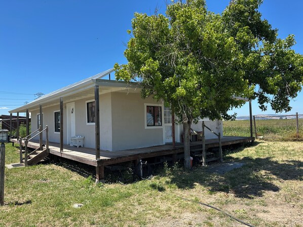A single-story house with a porch, a small deck, and a tree in front.