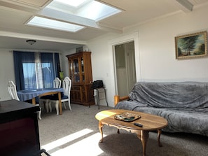 A living room with a sofa, a wooden coffee table, a dining table with chairs, a cabinet, and a painting on the wall.