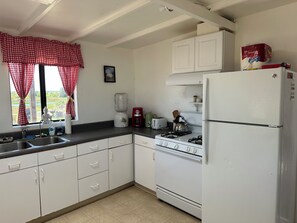 A kitchen with white cabinets, a refrigerator, a stove, a sink, and a window with red curtains.