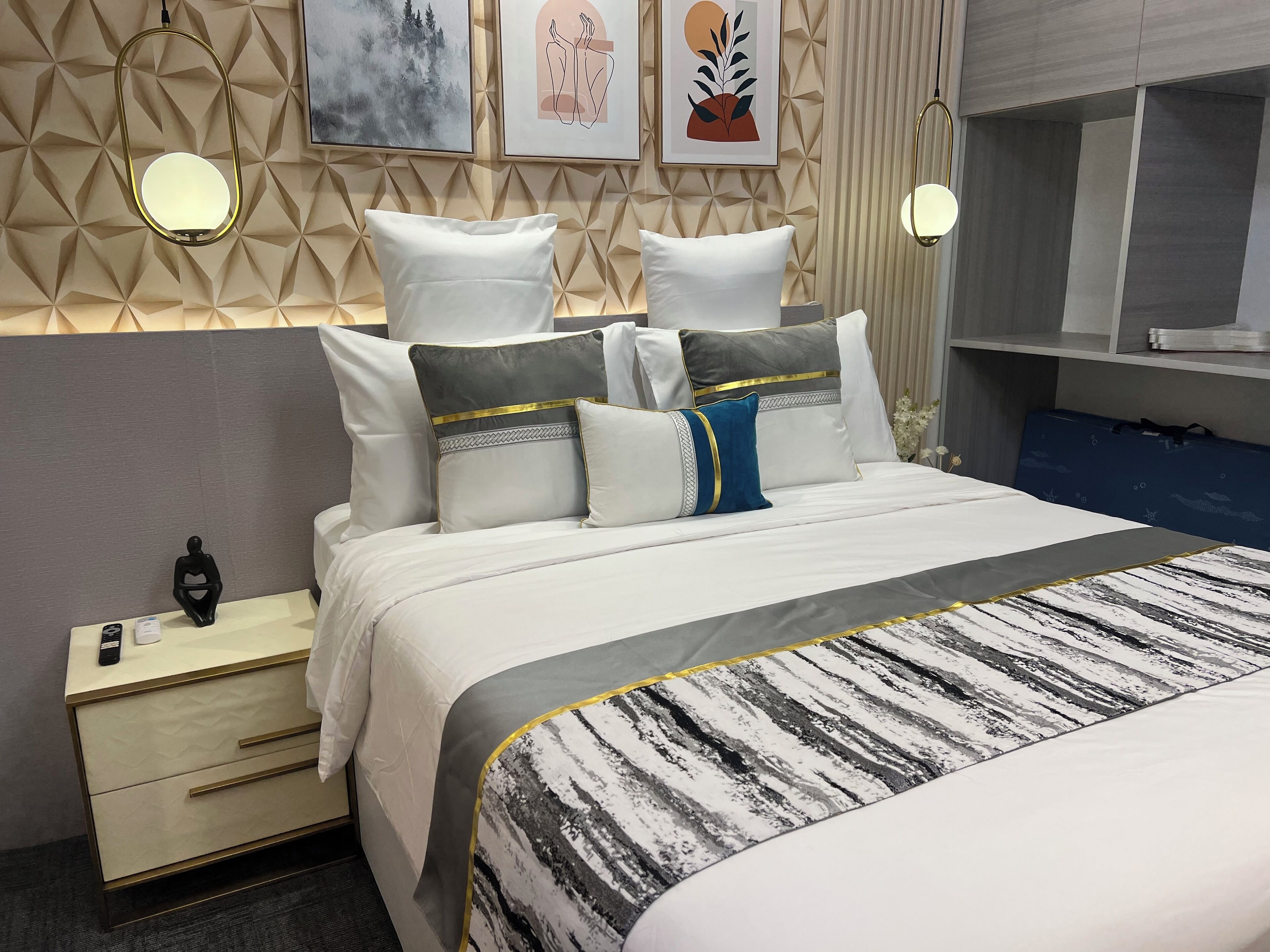 A modern hotel room with a neatly made bed, a bedside table with a lamp, and a wall with geometric patterns and artwork.