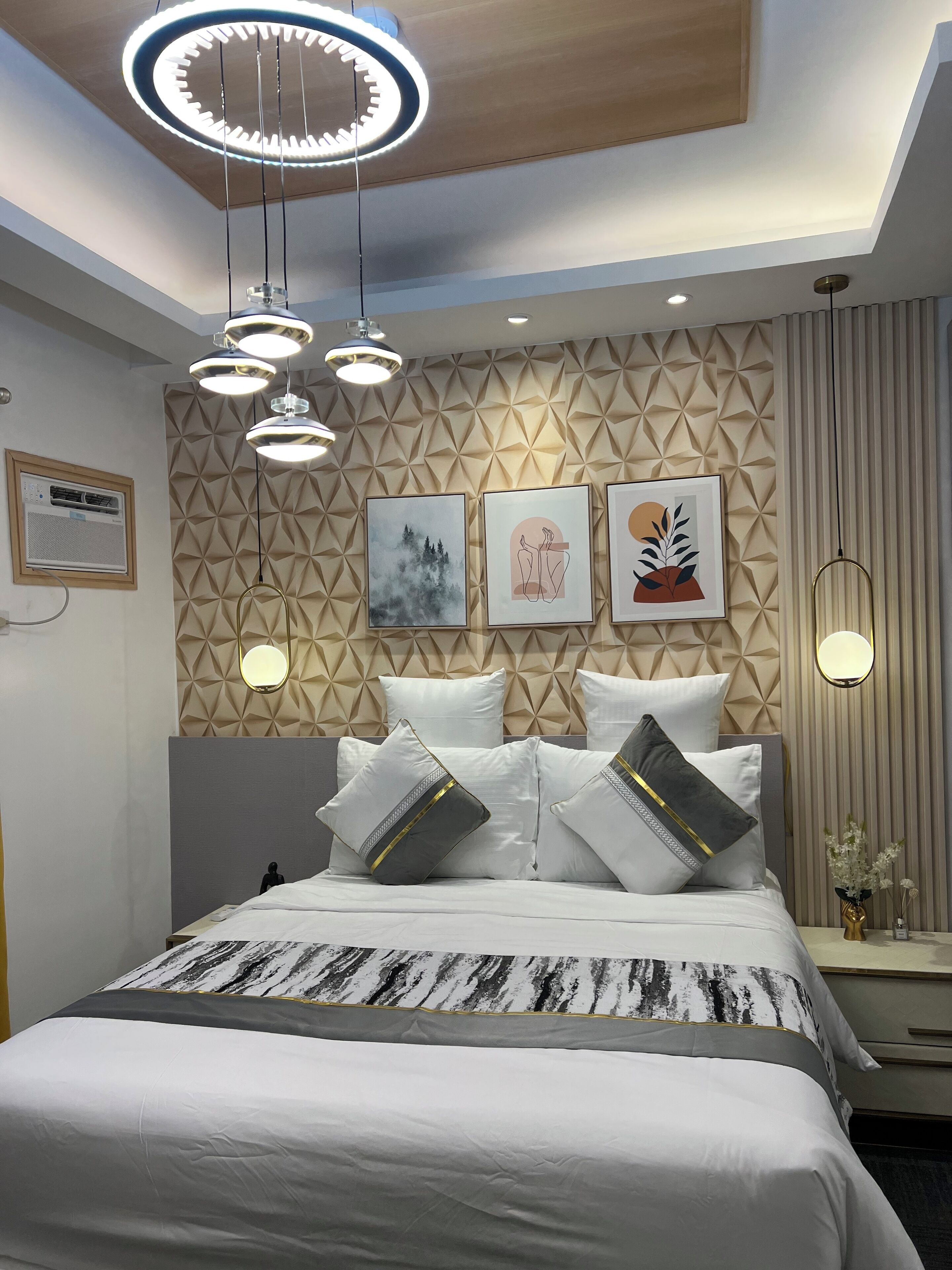 A modern bedroom with a geometric-patterned headboard, a bed with white bedding and decorative pillows, and a ceiling light fixture.