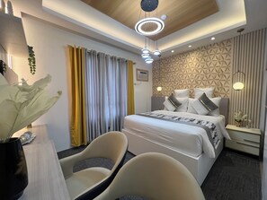 Ein modernes Hotelzimmer mit einem ordentlich bezogenen Bett, zwei Stühlen, einem Schreibtisch und einer Zierpflanze.
