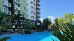 Una piscina con lettini e un'area giochi per bambini, circondata dal verde e da un edificio a più piani.