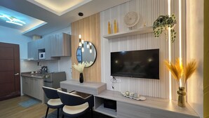 Una cucina moderna con forno a microonde integrato, zona pranzo con due sedie, TV montata su pannello di parete in legno e vaso con piante essiccate.
