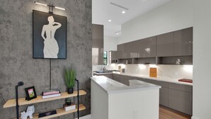 Una cocina moderna con gabinetes grises, una encimera blanca y una lámpara colgante sobre una obra de arte enmarcada.