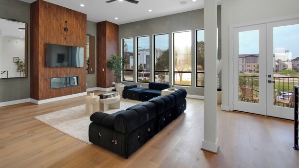 Un amplio salón con un sofá modular grande, un televisor de pantalla plana montado en una pared de madera, y un balcón con vistas a la ciudad.