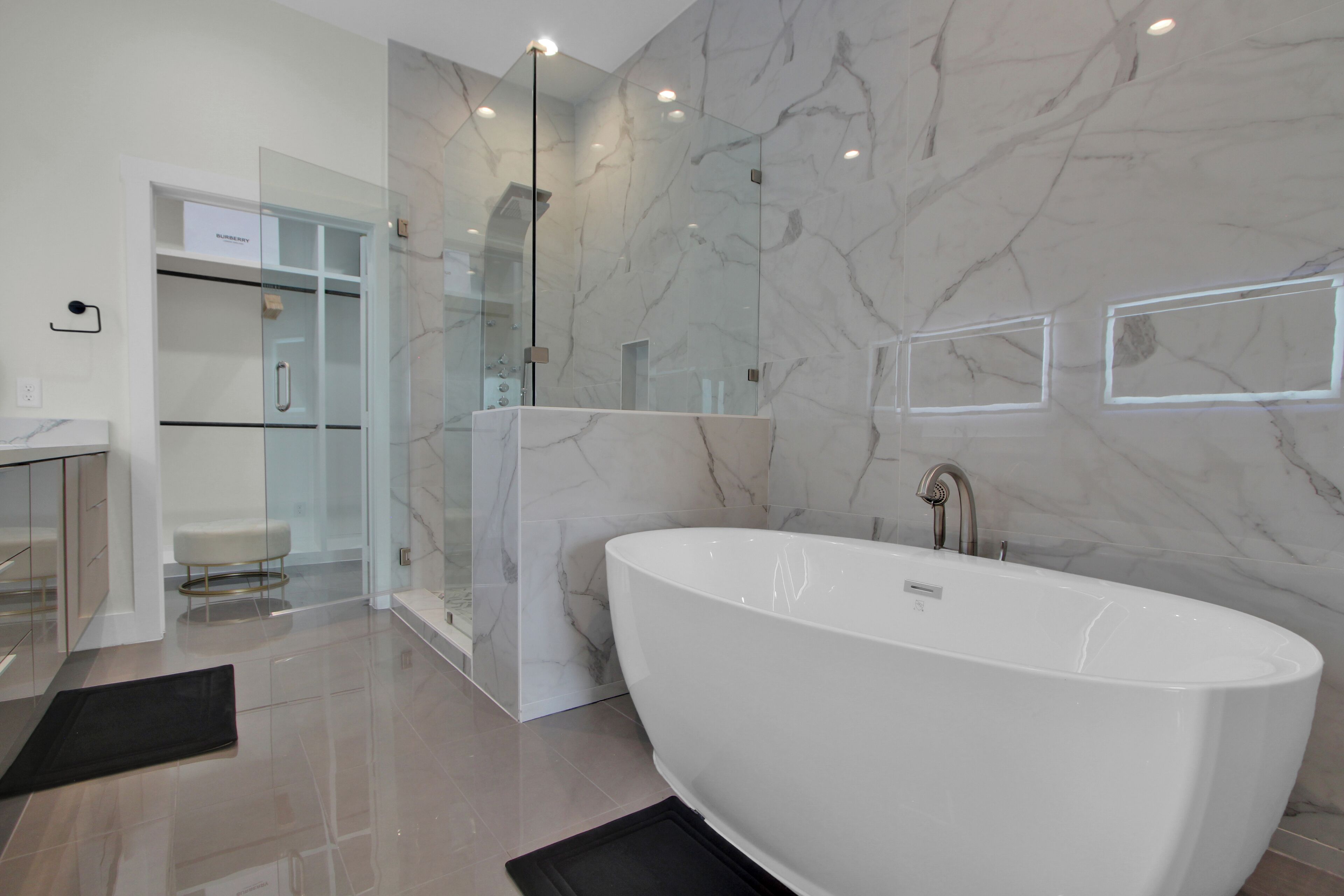 Een moderne badkamer met een vrijstaand bad, een douche met glazen wanden en marmeren wanden.