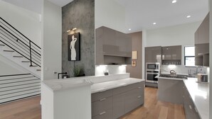Una cocina moderna con una isla central, electrodomésticos integrados y una escalera con barandillas negras.