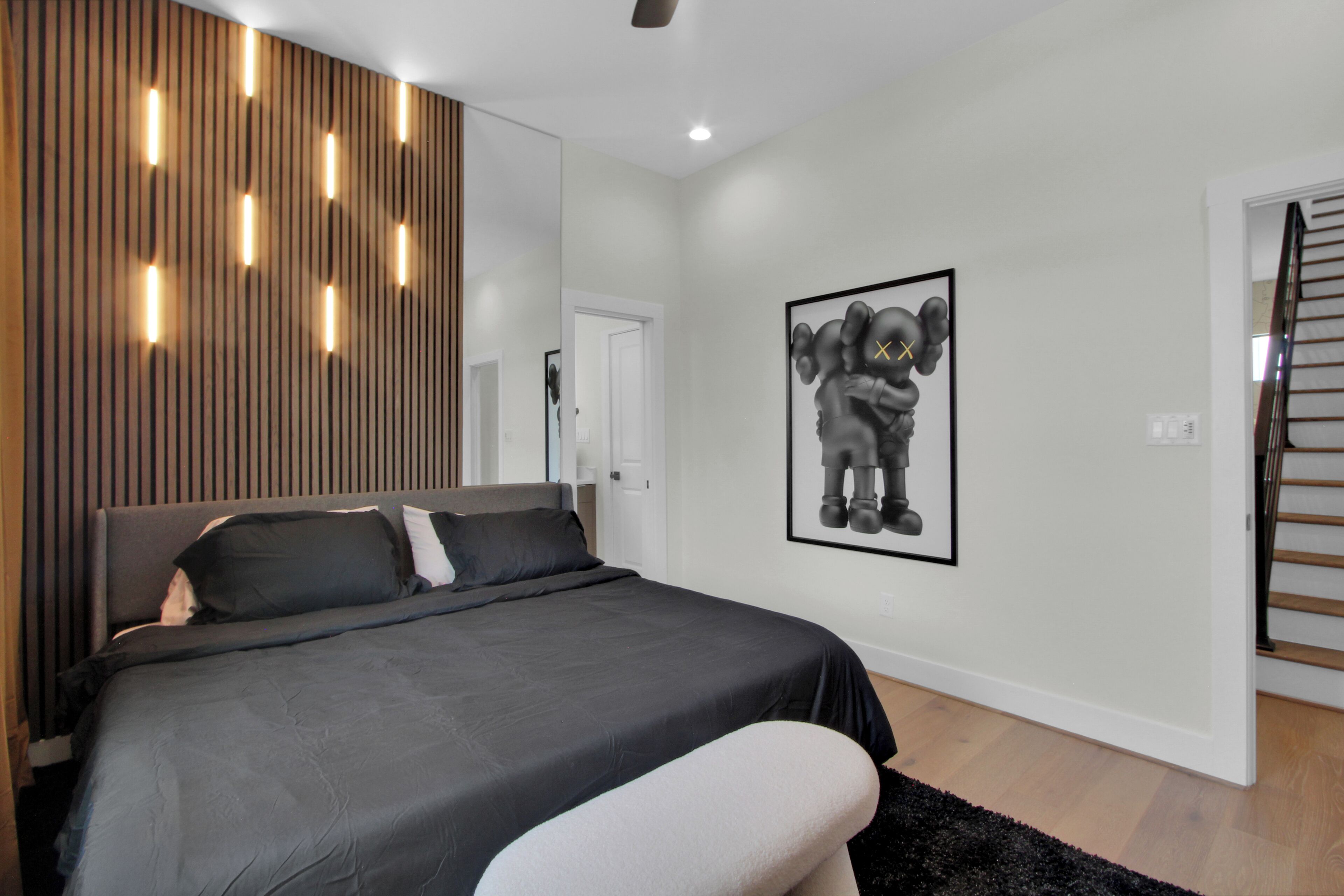 Ein modernes Schlafzimmer mit einem großen Bett, einer Wand aus Holzleisten, eingelassener Beleuchtung und einem gerahmten Bild.