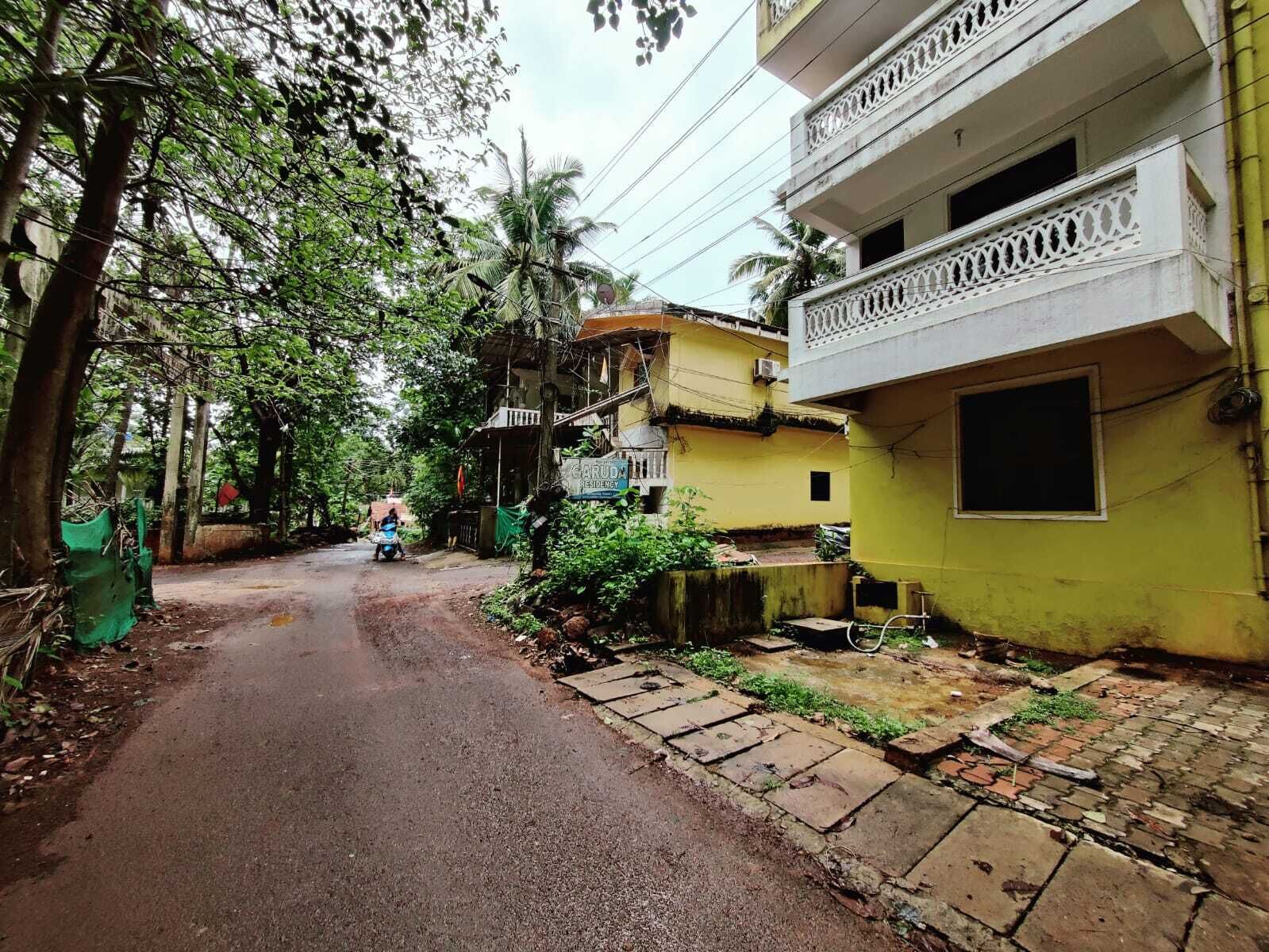 A narrow street flanked by residential buildings with balconies, a sign indicating a residential area, and a person walking on the road.