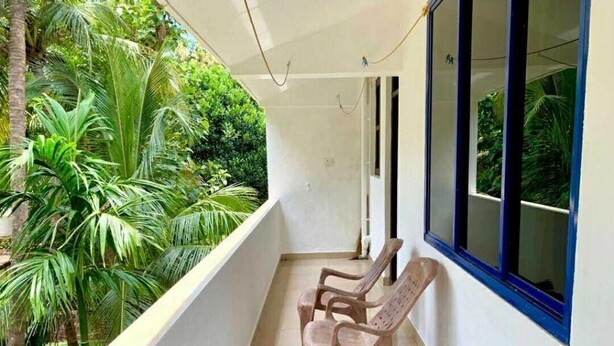 A balcony with two plastic chairs, a white wall, and a window overlooking greenery. - kkrishna apartments (Canacona)