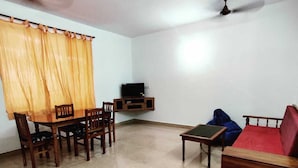 A living room with a dining table, chairs, a sofa, a TV on a stand, and a ceiling fan. - kkrishna apartments (Canacona)