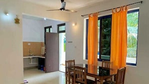 A dining area with a table and chairs, a ceiling fan, and a window with curtains. - kkrishna apartments (Canacona)