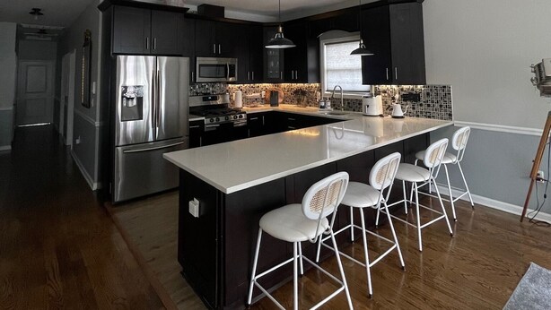 A modern kitchen with a large island, stainless steel appliances, and white bar stools.