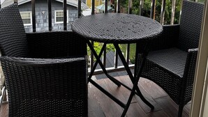 A balcony with wicker furniture and a view of houses and trees.