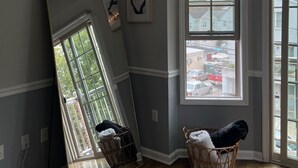 A room with a large mirror leaning against the wall, a window with a view of the outside, and a wicker basket with a blanket.
